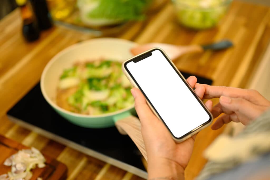 調理中のキッチンでスマートフォンを持つ手